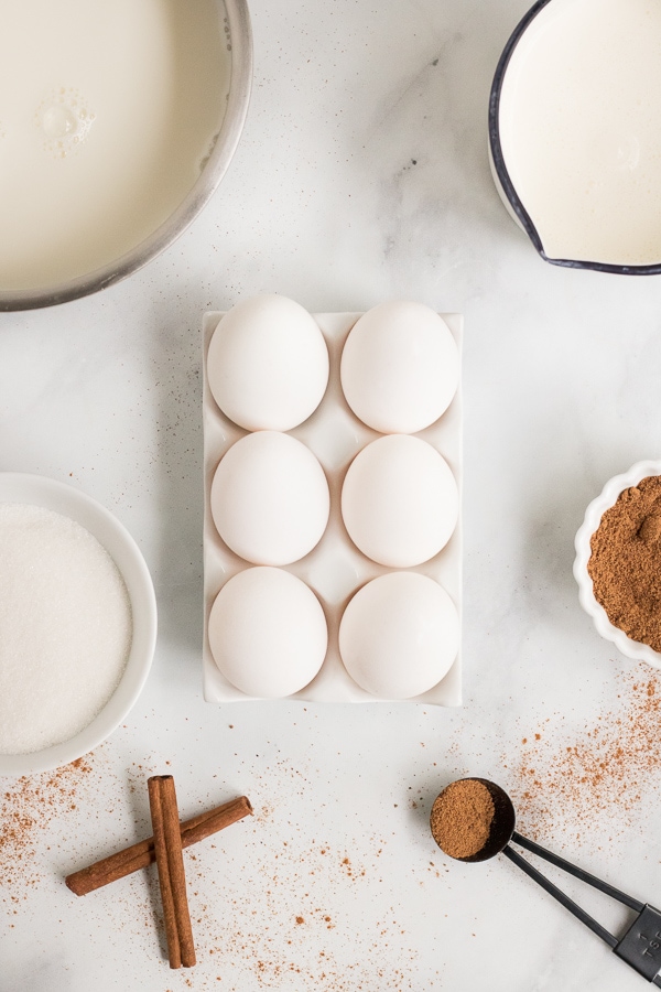 eggs, cinnamon, cream and milk sitting on a table ready to make eggnog