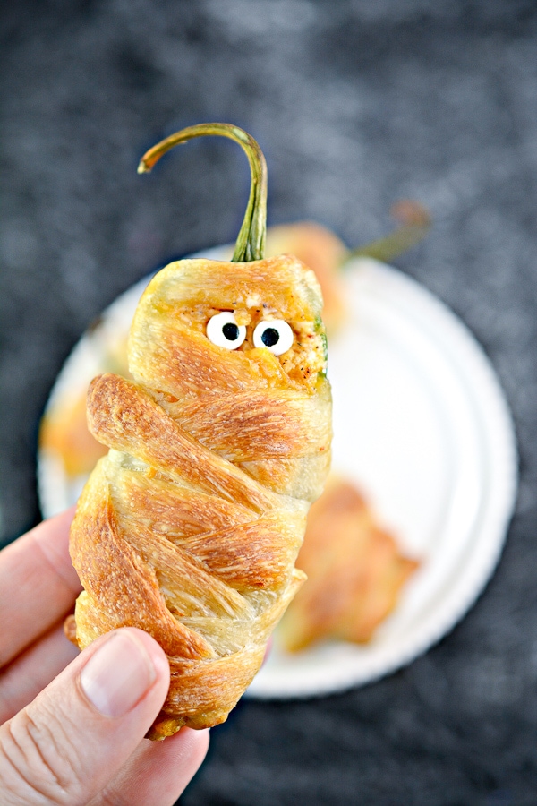 A hand holding a halloween themed jalapeno popper mummies