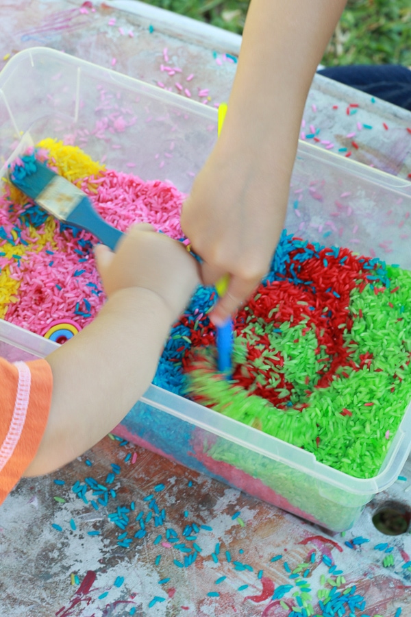 playing with sensory bin with dyed rainbow rice